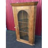 A limed oak corner cabinet, the angled cornice with beaded decoration above an arched astragal