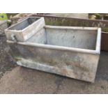 A rectangular galvanised trough with tubular rim, one end with compartment for former water