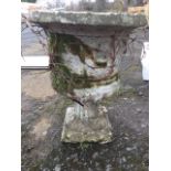 A composition stone urn, the body moulded with frieze of putti and swags, raised on a fluted socle