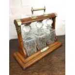 A late Victorian oak tantalus with silver plated leaf engraved mounts, the case holding three square