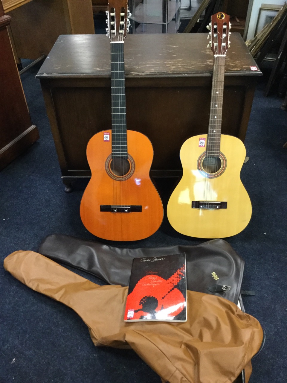 Two classical guitars, both with soft cases; and a classical guitar instruction book. (A lot)