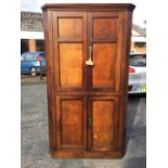 A nineteenth century oak corner cabinet with moulded cornice above four panelled doors enclosing