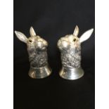 A silver plated salt & pepper modelled as hare's heads mounted with yellow glass eyes, raised on