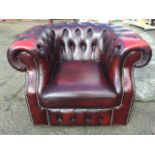 An ox-blood leather tub armchair with studded button upholstery and loose cushion, raised on