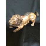 A cold painted bronze lion, the beast modelled in crouching position having oval pin cushion panel