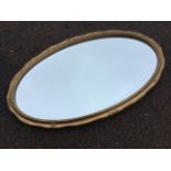 An oval gilt framed mirror, the bevelled plate in gesso mounted scrolled frame. (28in x 17.5in)