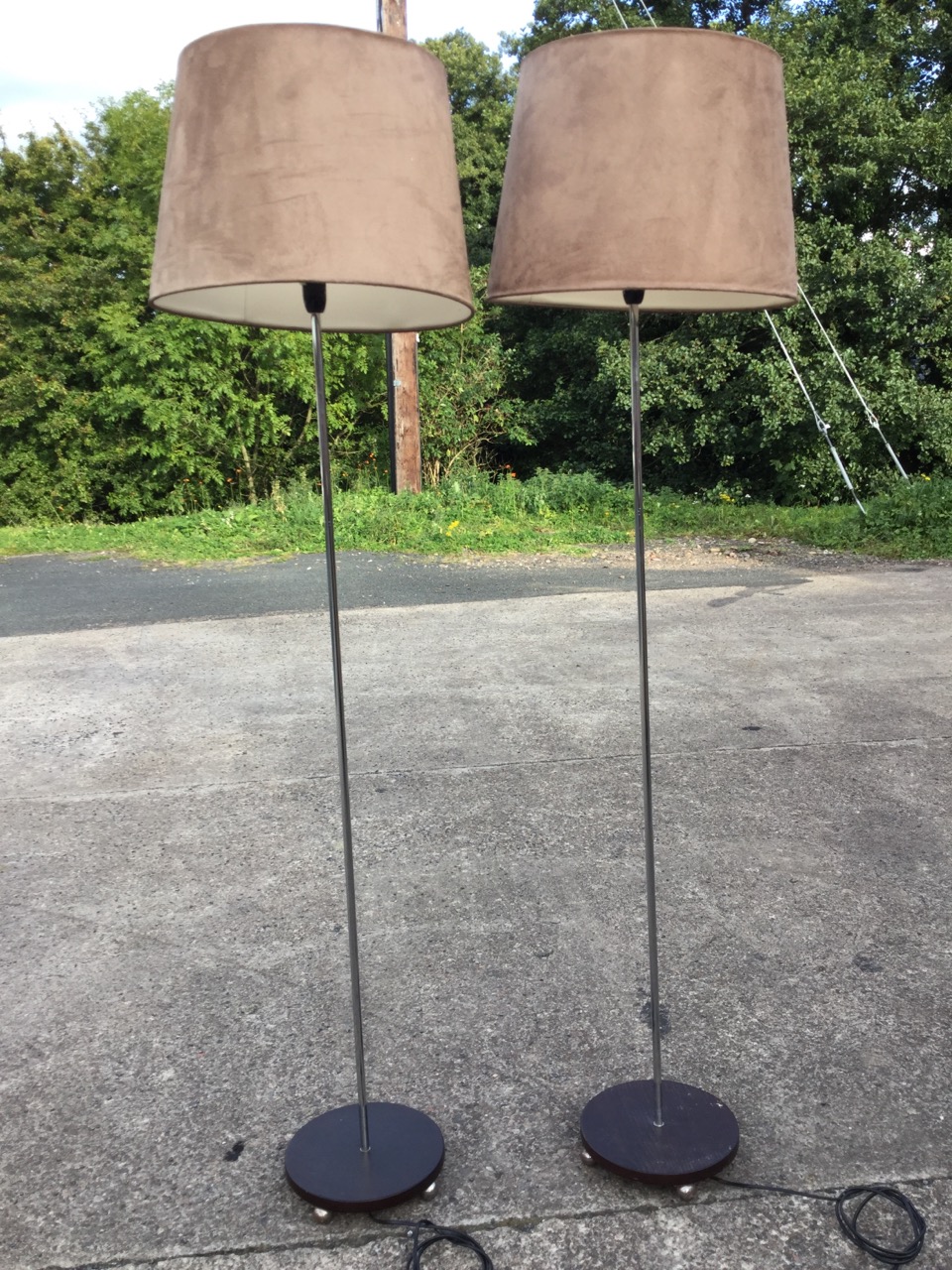 A pair of contemporary standard lamps with suede shades on chrome poles, the circular wood bases