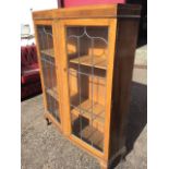 An oak bookcase cabinet with angled leaded glass doors framing a central moulded pillar, raised on