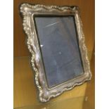 A hallmarked silver photo frame with waved scrolled embossed decoration on easel stand. (11in)