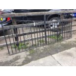 A pair of wrought iron driveway gates with scrolled panels framed by vertical bars in rectangular