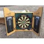 An unused Phil Taylor dartboard, the wallhanging cabinet fitted with circular Unicorn board,