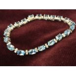 An 18ct gold blue topaz & diamond bracelet, with twenty-one oval claw set topaz stones weighing