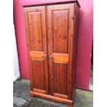 A stained pine wardrobe with two fielded panelled doors enclosing shelf and hanging space, raised on