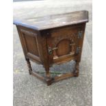 An oak side cabinet with angled top above an arched leaf carved door, with panelled sides raised