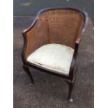 An Edwardian bergere armchair with rounded cane back above a sprung upholstered seat, raised on