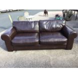 A large leather upholstered three-seater sofa, with loose cushions and panelled stitching, raised on