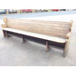 A long Victorian pine pew, the tongue & groove boarded back above a plank seat, the shaped ends