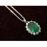 An 18ct white gold Zambian emerald & diamond pendant, the oval claw set emerald framed by border