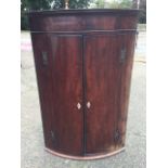 A barrel fronted nineteenth century mahogany corner cabinet with moulded cornice above a plain