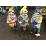 A set of three colourful garden gnomes, the bearded composition stone figures seated on logs. (23in)