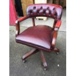 A reproduction oxblood leather upholstered captains chair, the rounded button back with studded
