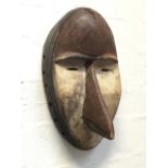 A tribal mask, the oval wood carved face with beak/nose, in original paint with holes to rim. (