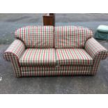 A contemporary two seater sofa with loose cushions, upholstered in tartan, raised on bun feet. (