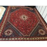 An Iranian carpet with busy red field woven with birds, vases, flowers etc., around a lozenge shaped