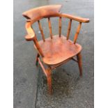 An elm captains chair with rounded smokers bow spindleback above a solid seat, raised on turned legs