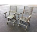 A pair of teak folding garden armchairs with slatted backs and seats and platform arms, raised on
