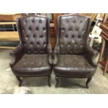 A pair of leather button upholstered wing armchairs, the high backs above bowfronted seats and