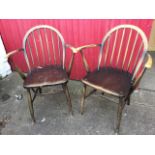 A pair of Ercol elbow chairs with hooped spindlebacks and rounded tapering arms above solid seats,