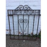 A rectangular wrought iron garden gate with scrolled decoration and twisted bars, the banner reading