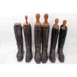 Three pairs of vintage black leather hunting boots, each with a set of wooden trees,
