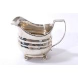 George III silver cream jug of bellied form with reeded rim, angular handle, on four ball feet.