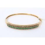 18ct gold emerald and diamond hinged bangle with a line of round mixed cut emeralds flanked by a