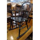 An ebonised wood framed wheel back elbow rocking chair with solid seat and turned supports