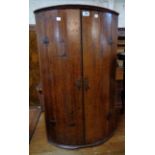 A 23" antique polished oak wall hanging bow front corner cabinet with three shelves enclosed by a