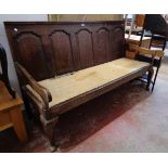 A 5' 11" antique oak bench with five panel back, open armrests and remains of seat webbing, set on