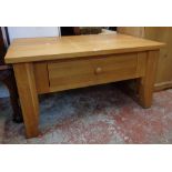 A 35 1/2" modern polished oak coffee table with single drawer, set on heavy shaped square legs