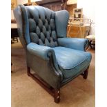 A late 20th Century wing back armchair upholstered in blue button back leather, set on polished wood