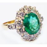 A marked 18ct. yellow metal ring, set with central 2.16ct. oval emerald within a diamond encrusted