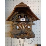 A 20th Century carved wood cuckoo clock with revolving figures to top and triple cast metal fur cone