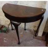 A 32" 1920's flame mahogany and cross banded demi-lune fold-over card table, set on slender cabriole