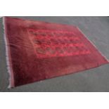 A Pakistani Bokhara rug with three rows of seven guls within a wide repeat border, black on red -