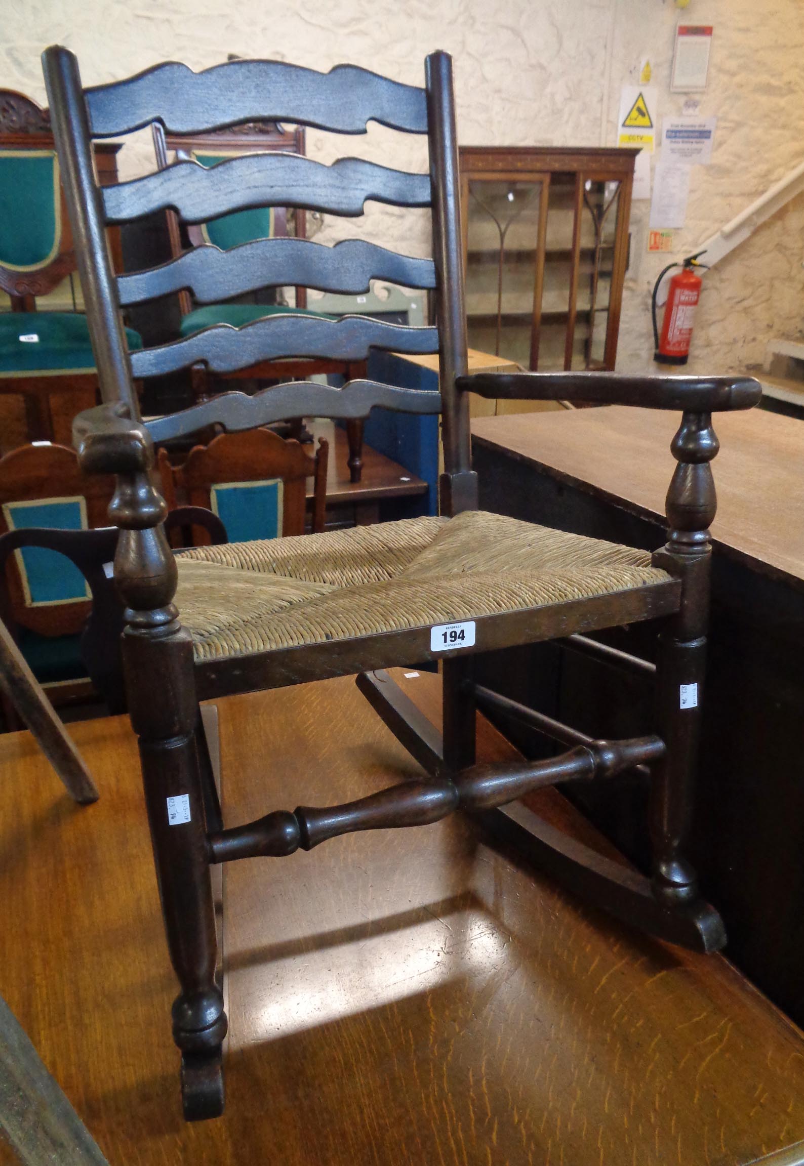 A 20th Century stained elm ladder back rocking chair with woven rush seat and turned supports