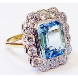 A marked 18ct. yellow metal ring, set with 3.85ct. emerald cut aquamarine within a fourteen stone