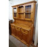 A 4' 7 1/2" modern stained pine two part dresser with shelves and glazed cupboard to top, over three