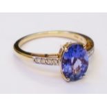 A hallmarked 750 yellow metal ring, set with central oval tanzanite with tiny diamonds to shoulders
