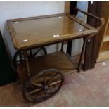 A vintage stained wood tea wagon with glass inset tray top and spoked wheels